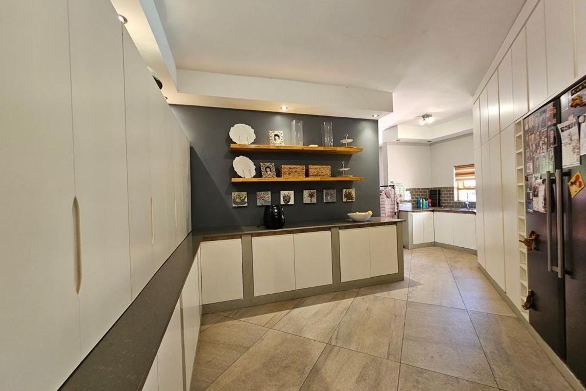 Modern kitchen featuring extensive white cabinetry, dark stone countertops, floating timber shelving, and large format floor tiles.