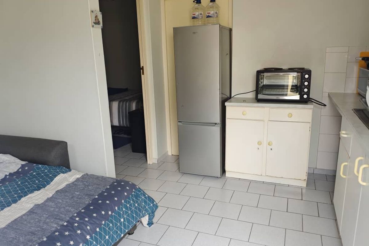 A compact kitchenette area featuring basic cabinetry, tiled flooring, and direct access to an adjacent bedroom space.