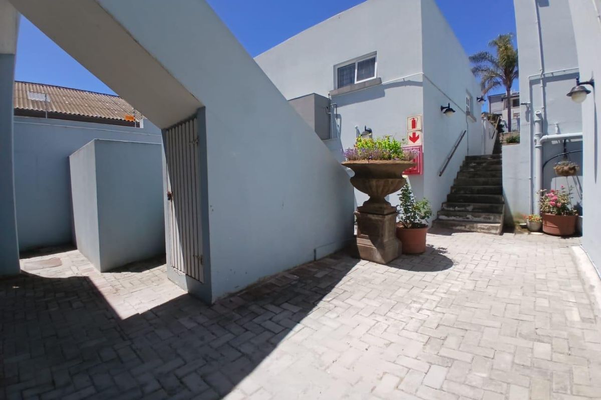 A paved courtyard area featuring an external staircase, built-in storage structure, and exterior lighting, providing access to the upper levels of the townhouse.
