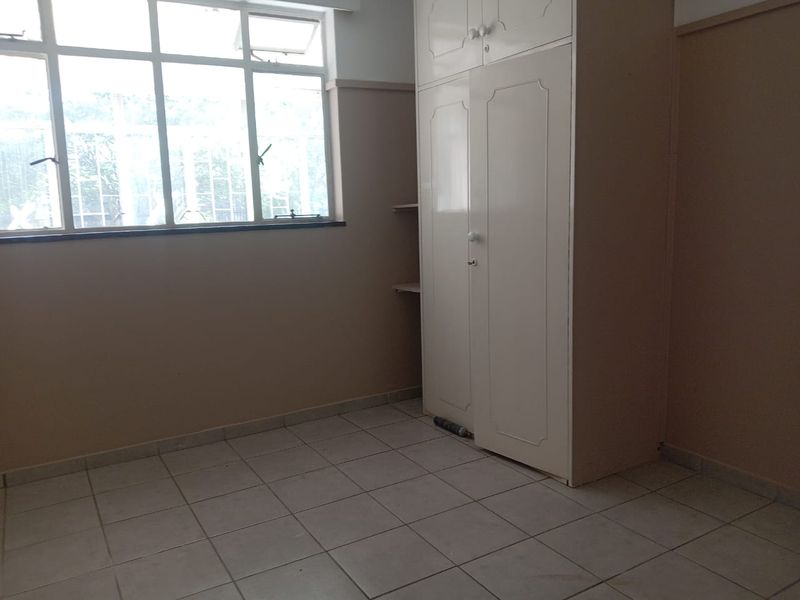A vacant bedroom featuring tiled flooring, a large window for natural light, and a built-in wardrobe with overhead storage.