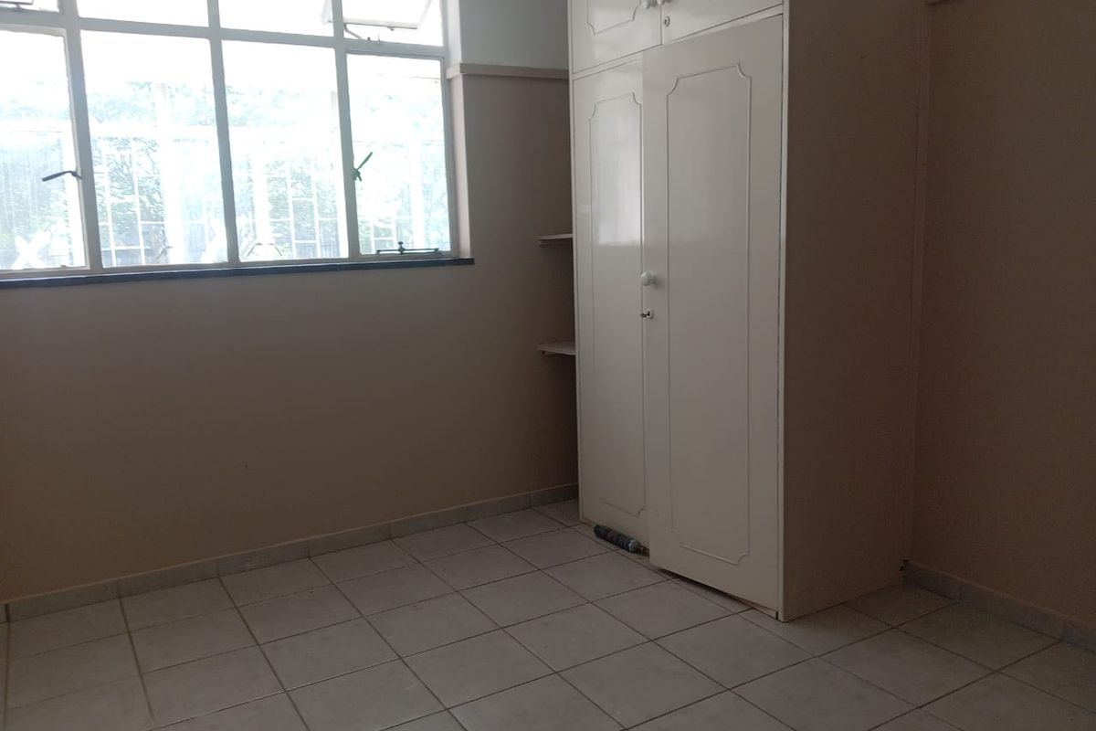 A vacant bedroom featuring tiled flooring, a large window for natural light, and a built-in wardrobe with overhead storage.