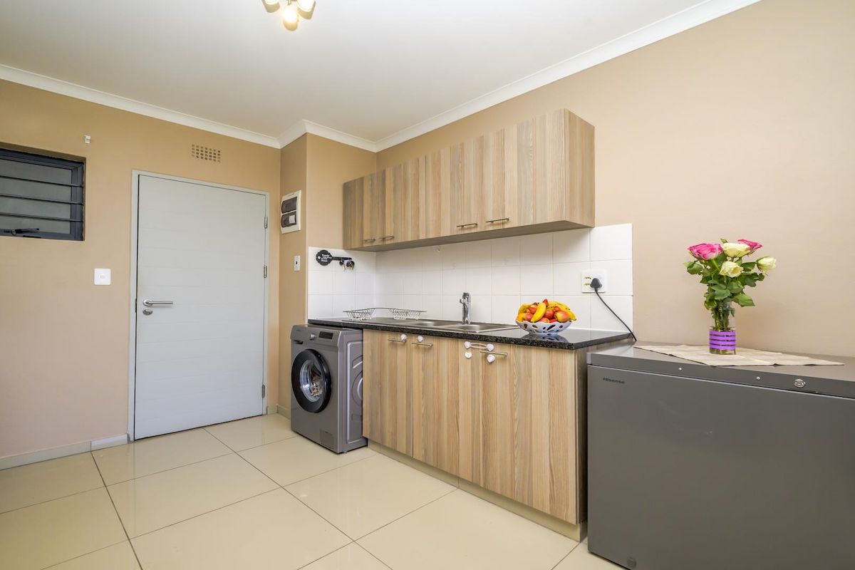 A functional kitchen featuring laminate cabinetry, granite countertops, tiled flooring, and a tiled splashback, providing a clean and practical workspace.