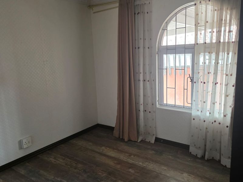 A vacant bedroom featuring wood-look laminate flooring, an arched window with security bars, and recessed ceiling lighting.