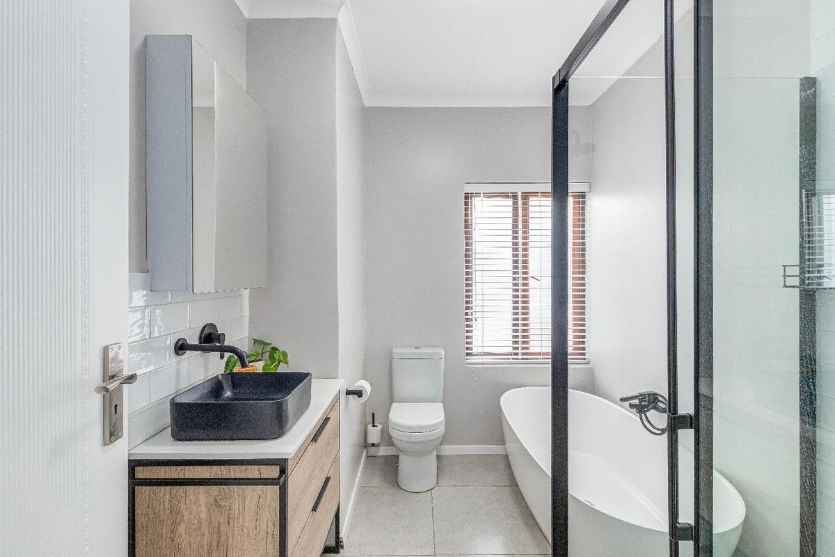 Modern bathroom featuring a freestanding bathtub, walk-in shower with black frame, vanity with vessel sink, and neutral tiled finishes.