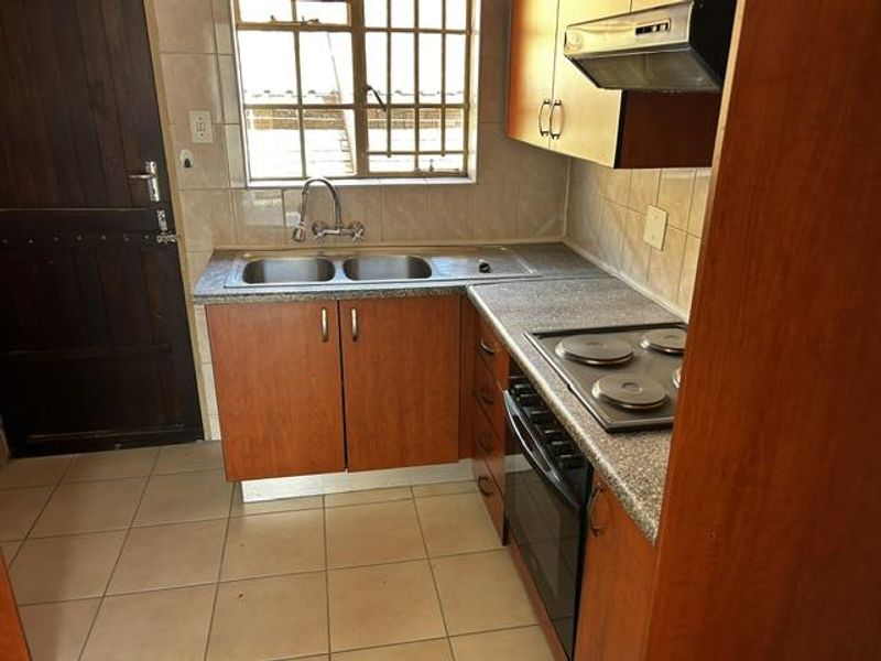 A functional kitchen featuring laminate cabinetry, a double sink, built-in oven, electric hob, and tiled flooring with security bars on the window.