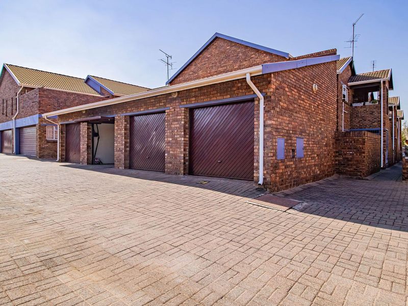 Exterior view of a residential apartment complex featuring brick facades, tiled roofs, and multiple garage units with a paved driveway.