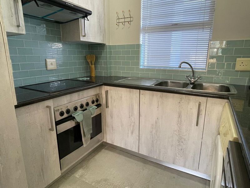 A functional kitchen featuring light wood-grain cabinetry, dark laminate countertops, a subway tile backsplash, and integrated stainless steel appliances.