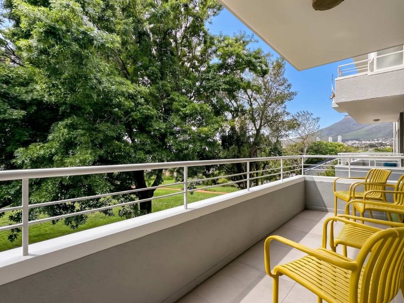 A well-maintained balcony featuring tiled flooring and a metal balustrade, offering pleasant views of surrounding greenery and mountain scenery.