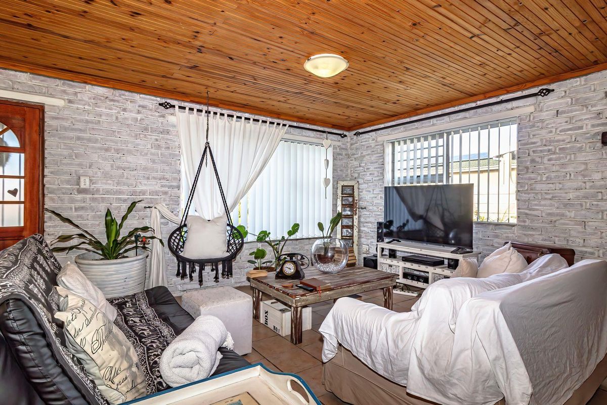 A cozy living room featuring exposed brick walls, a warm timber tongue and groove ceiling, and tiled flooring with security-fitted windows.