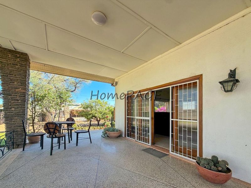 A covered patio area featuring a stone-clad pillar, sliding glass doors with security gates, and an exterior wall light.