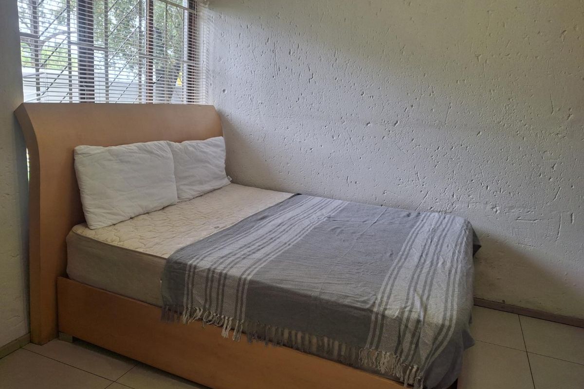 A bedroom featuring tiled flooring, textured walls, and a window fitted with security bars and venetian blinds.