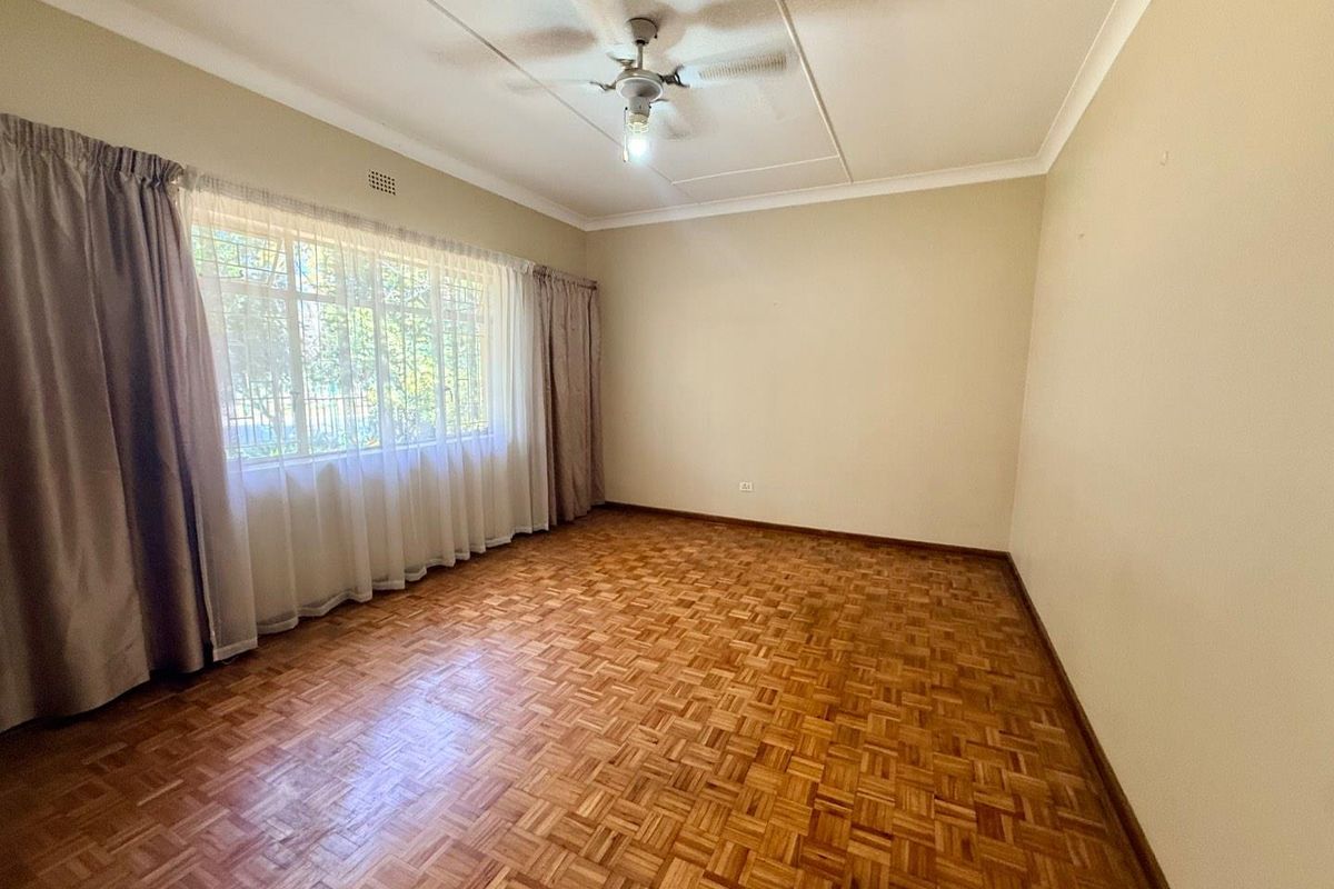 A spacious, empty bedroom featuring classic parquet flooring, a ceiling fan, and large windows with security bars, offering a neutral canvas for personalization.