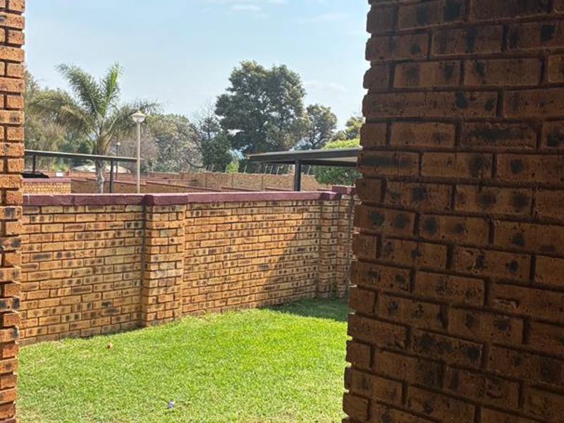 A covered patio area featuring brick walls and paved flooring, overlooking a private garden space within the cluster complex.