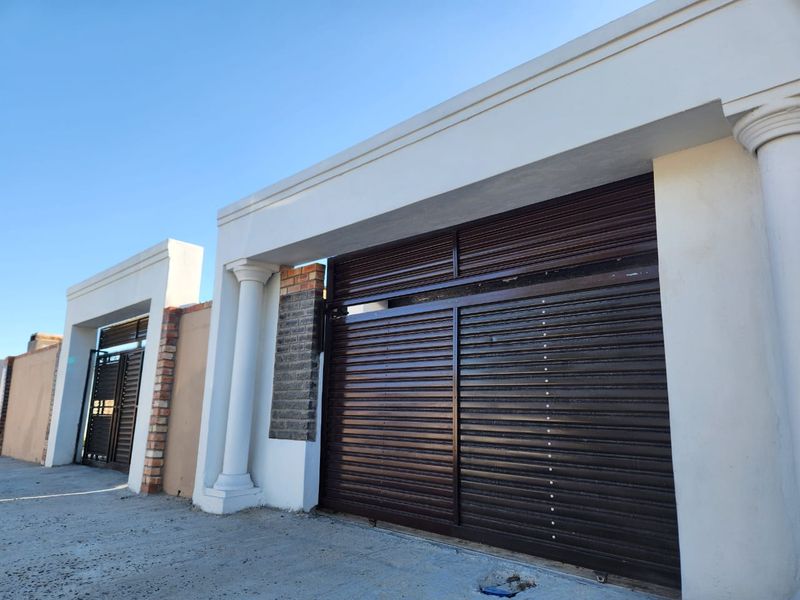 Front exterior view featuring a secure sliding metal gate, decorative concrete columns, and brick masonry accents.