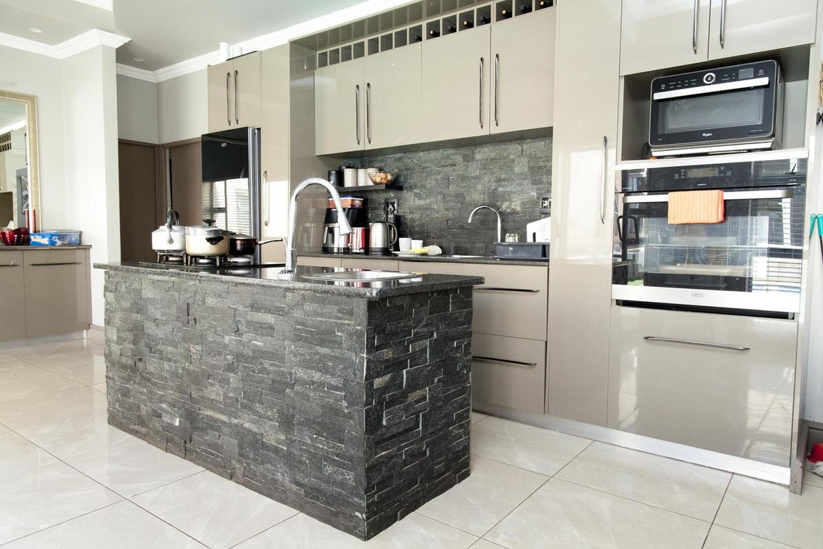 Modern kitchen featuring high-gloss cabinetry, a stone-clad island with a sink, built-in oven, microwave, and tiled flooring.