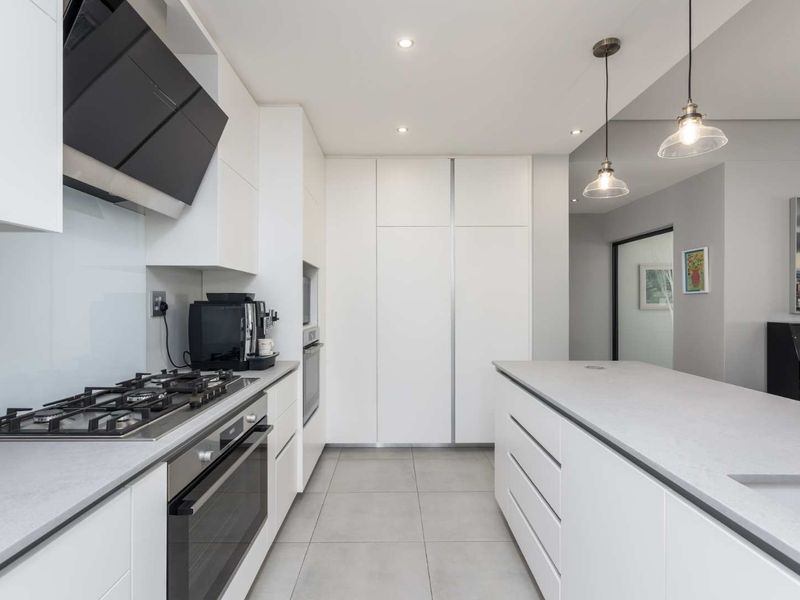 Modern, high-end kitchen featuring sleek white cabinetry, stone countertops, a central island, integrated appliances, and contemporary pendant lighting.