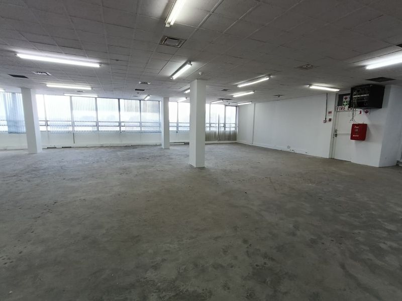 Spacious open-plan office area featuring a suspended ceiling, fluorescent lighting, and large windows with vertical blinds, ready for custom fit-out.