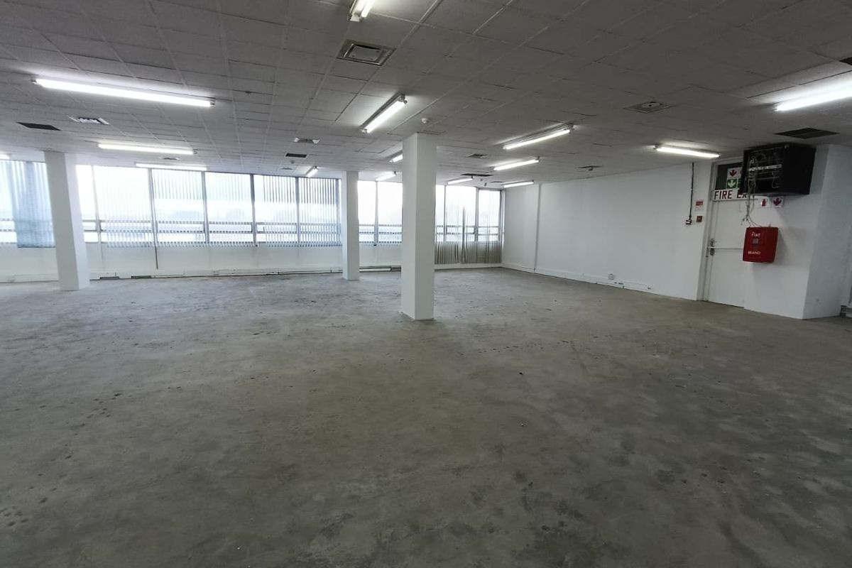 Spacious open-plan office area featuring a suspended ceiling, fluorescent lighting, and large windows with vertical blinds, ready for custom fit-out.