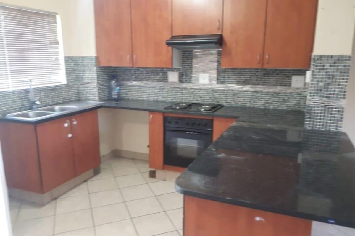 A functional kitchen featuring wooden cabinetry, dark granite countertops, a built-in oven, gas hob, extractor fan, and a double sink with mosaic tile backsplash.