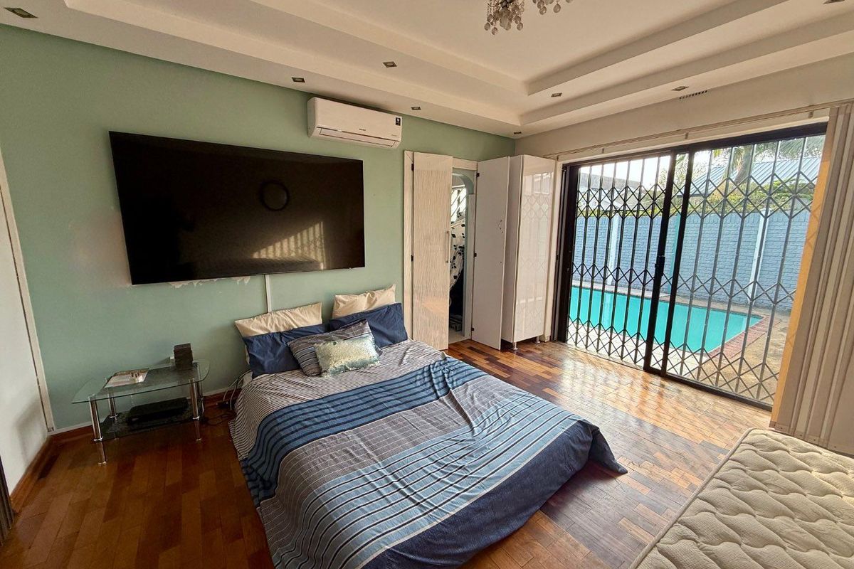 Spacious bedroom featuring wooden flooring, recessed ceiling lighting, air conditioning unit, and sliding glass doors with security gates leading to the pool area.
