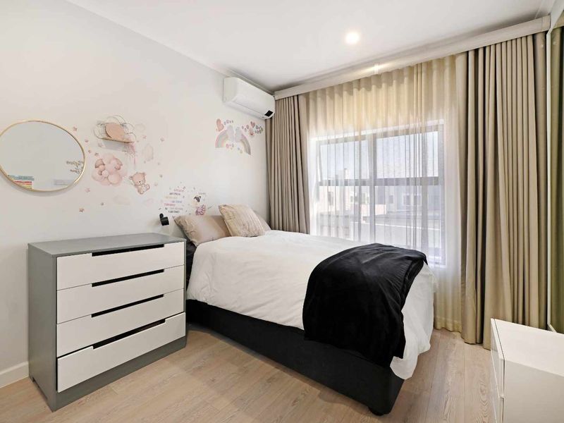 A well-maintained bedroom featuring light laminate flooring, a split-system air conditioner, and floor-to-ceiling curtains covering the window.