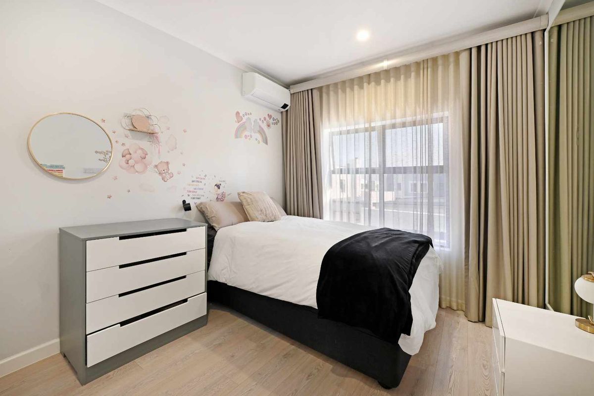 A well-maintained bedroom featuring light laminate flooring, a split-system air conditioner, and floor-to-ceiling curtains covering the window.