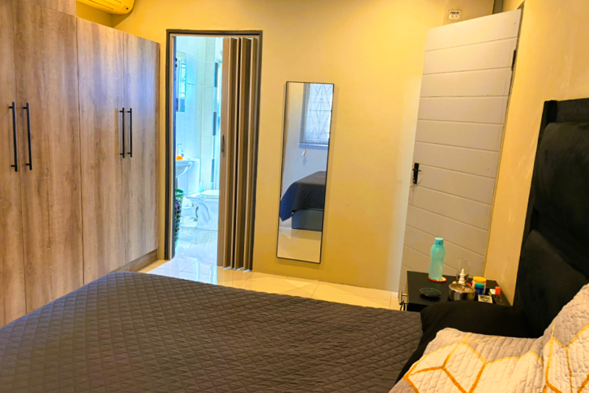 A bedroom featuring built-in wooden wardrobes, an en-suite bathroom with a folding door, and a wall-mounted air conditioning unit.