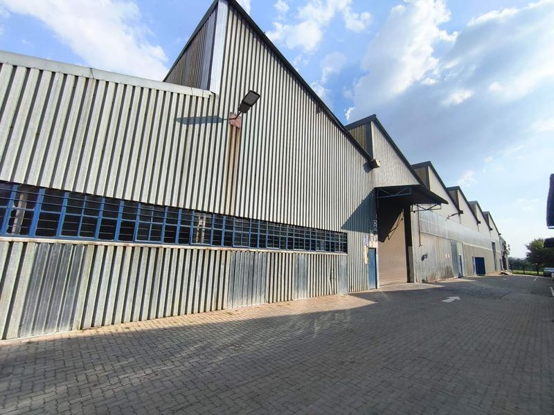 Industrial warehouse facility featuring corrugated metal cladding, multiple roller shutter access points, and a paved driveway area.