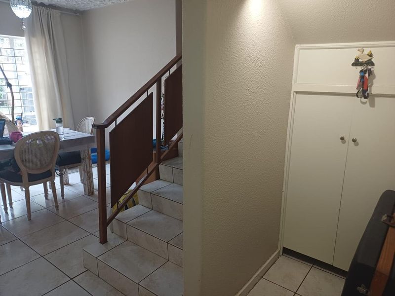 A functional hallway area featuring a staircase with a wooden railing, tiled flooring, and a built-in storage cupboard.