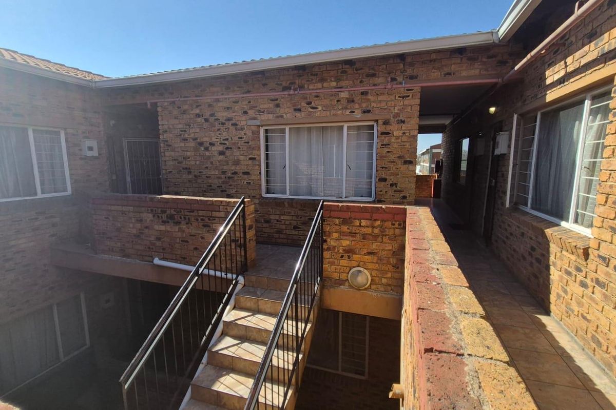 Exterior view of an apartment complex featuring face brick construction, a central metal staircase, and tiled walkways connecting the units.