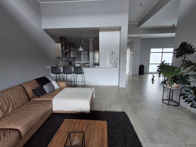 Spacious open-plan living area featuring a modern kitchen with a breakfast bar, tiled flooring, and neutral wall finishes throughout.