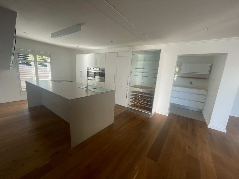 Modern open-plan kitchen featuring a large central island, integrated appliances, hardwood flooring, and an adjacent scullery area with ample storage.