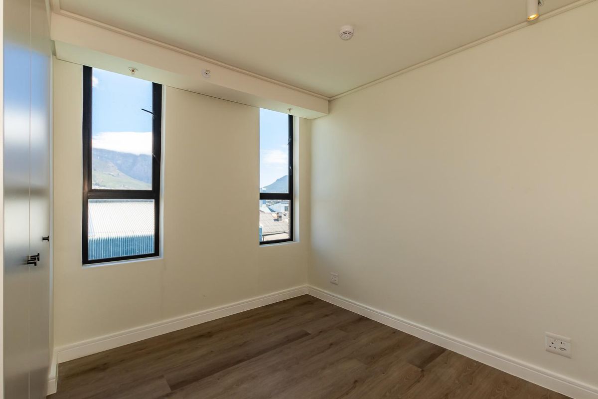 A bright, empty bedroom featuring modern laminate flooring, built-in cupboards, and large windows offering natural light and mountain views.