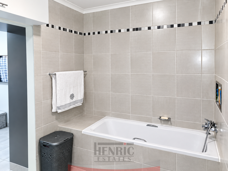 A clean, modern bathroom featuring a built-in bathtub with chrome fixtures, tiled walls with a decorative border, and a convenient recessed storage niche.