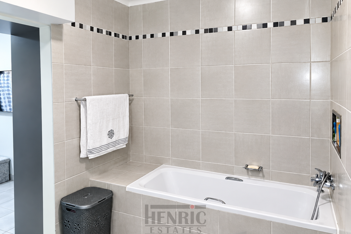 A clean, modern bathroom featuring a built-in bathtub with chrome fixtures, tiled walls with a decorative border, and a convenient recessed storage niche.