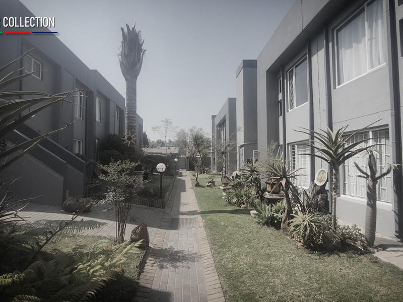 A view of the communal garden area between townhouse units, featuring a paved walkway, established landscaping, and exterior building facades.
