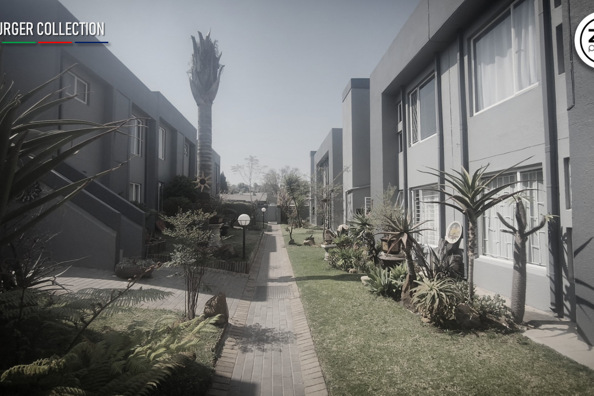 A view of the communal garden area between townhouse units, featuring a paved walkway, established landscaping, and exterior building facades.
