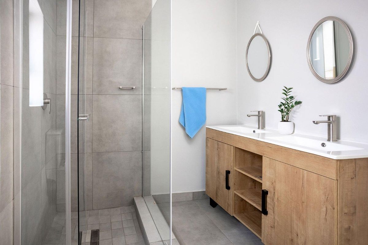 Modern bathroom featuring a double vanity with wood-look cabinetry, integrated sinks, and a spacious walk-in shower with large-format grey tiling.