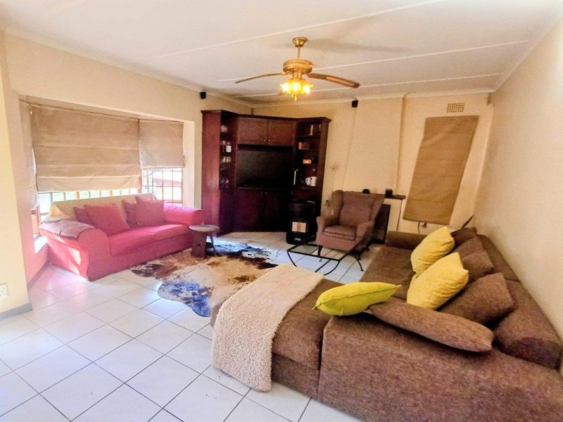 A spacious living room featuring tiled flooring, a ceiling fan, and built-in wooden cabinetry for storage and media display.
