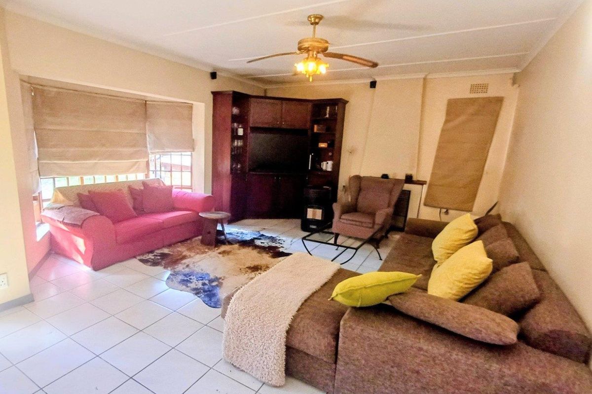 A spacious living room featuring tiled flooring, a ceiling fan, and built-in wooden cabinetry for storage and media display.