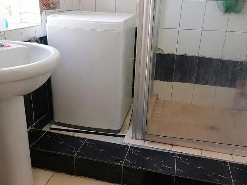 A functional bathroom featuring a pedestal basin and a shower enclosure with tiled finishes, requiring some maintenance and cosmetic updates.