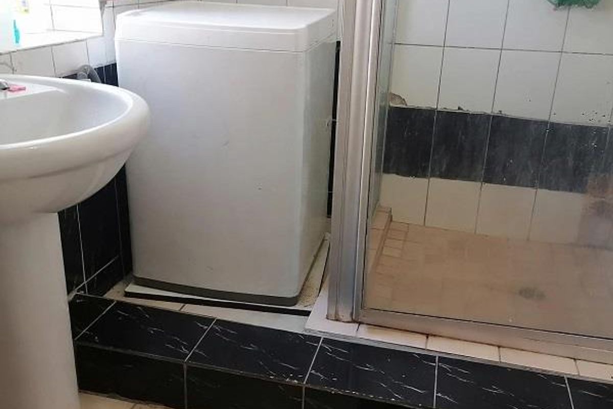 A functional bathroom featuring a pedestal basin and a shower enclosure with tiled finishes, requiring some maintenance and cosmetic updates.