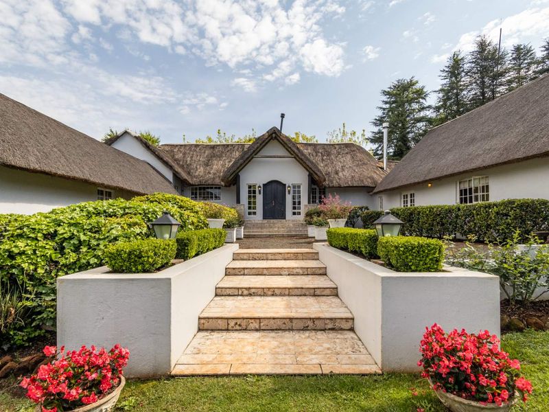 A charming farmhouse entrance featuring a classic thatched roof, stone steps, and well-maintained retaining walls leading to a welcoming double-door entryway.