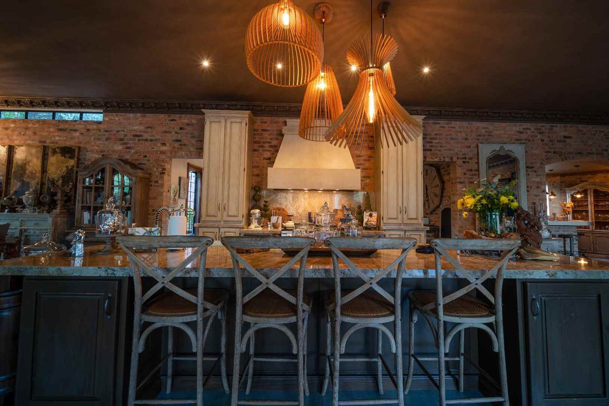 A rustic-style kitchen featuring exposed brick walls, custom cabinetry, a large stone-topped island, and decorative pendant lighting.