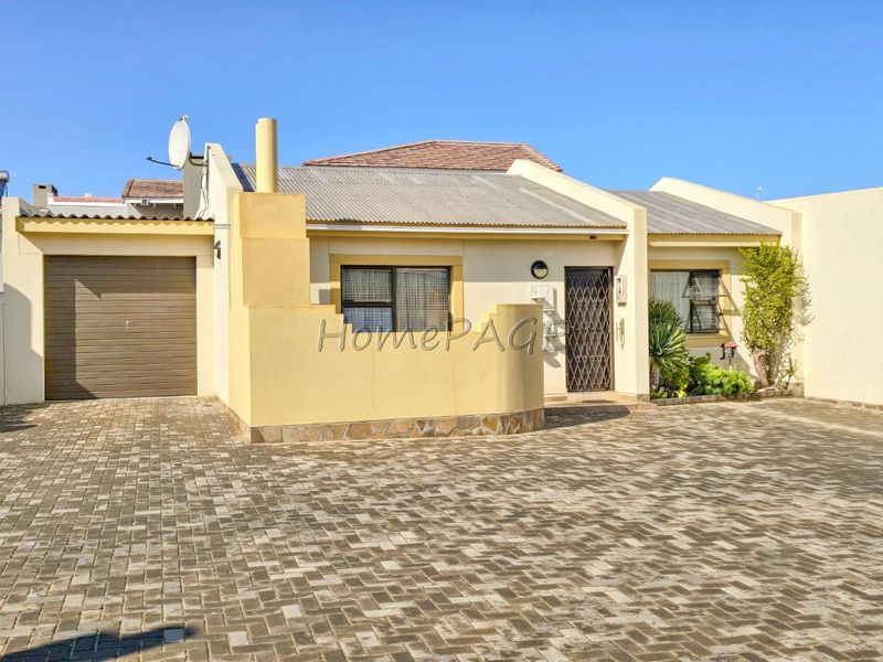 Front elevation of a townhouse featuring a paved driveway, single garage, and secure entrance with a security gate.