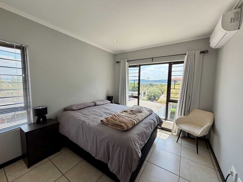 A well-lit bedroom featuring tiled flooring, a wall-mounted split-system air conditioner, and large windows with security bars offering an elevated view.