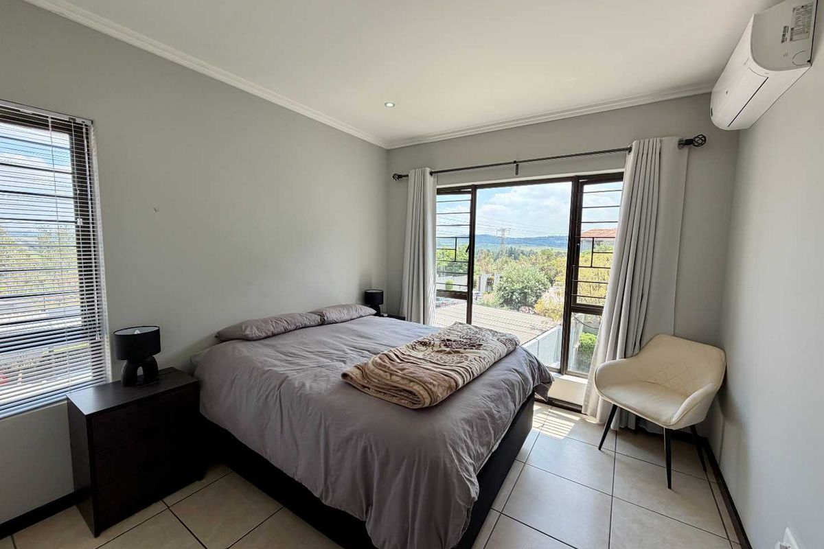 A well-lit bedroom featuring tiled flooring, a wall-mounted split-system air conditioner, and large windows with security bars offering an elevated view.