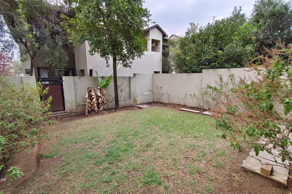 A private rear garden featuring a lawn area, perimeter boundary walls, and a pedestrian access gate.
