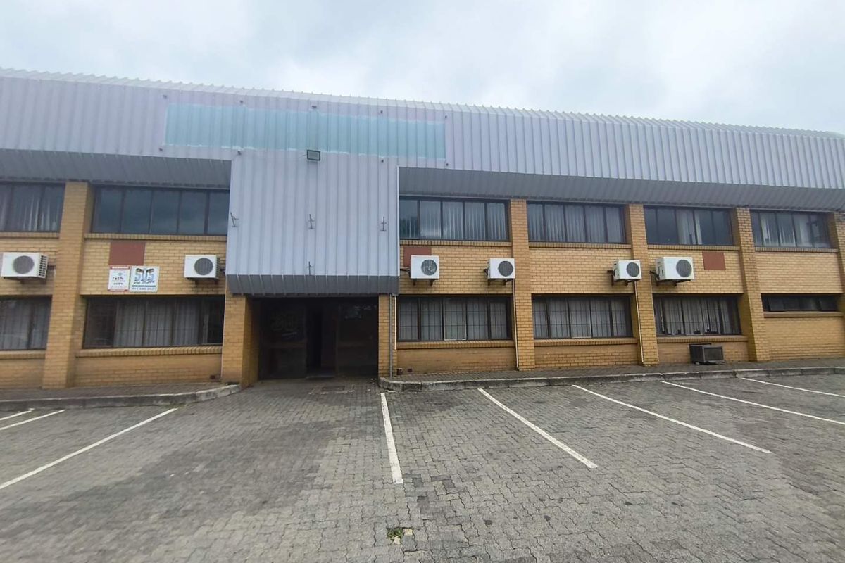 Front elevation of an industrial building featuring a brick facade, metal cladding, and a paved parking area with multiple external air conditioning units.