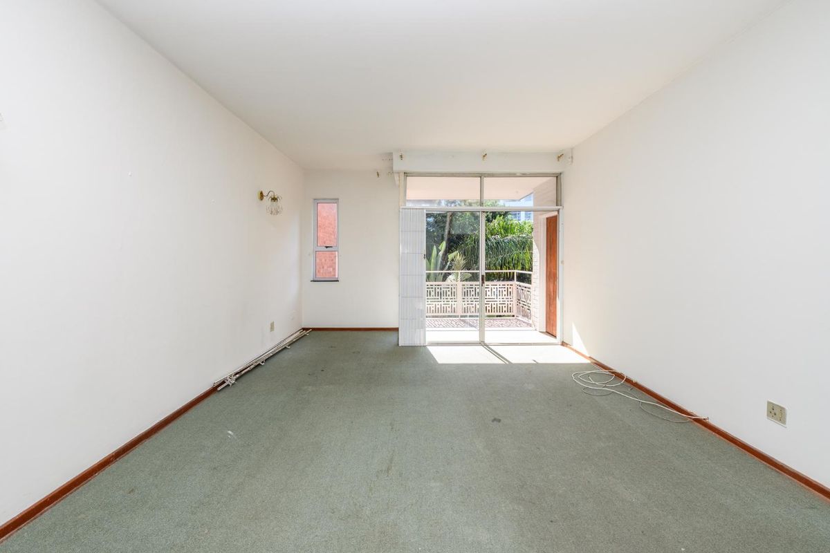 An empty living room featuring wall-to-wall carpeting, sliding glass doors leading to a balcony, and a small side window.